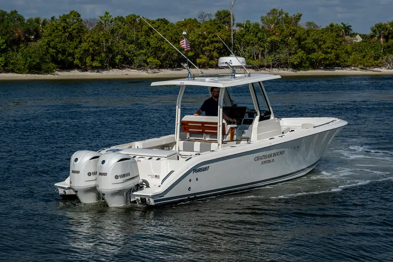 Slide: The Image of 2021 Pursuit S 288 Sport boat cruising on a calm lake with lush green shoreline. - 16