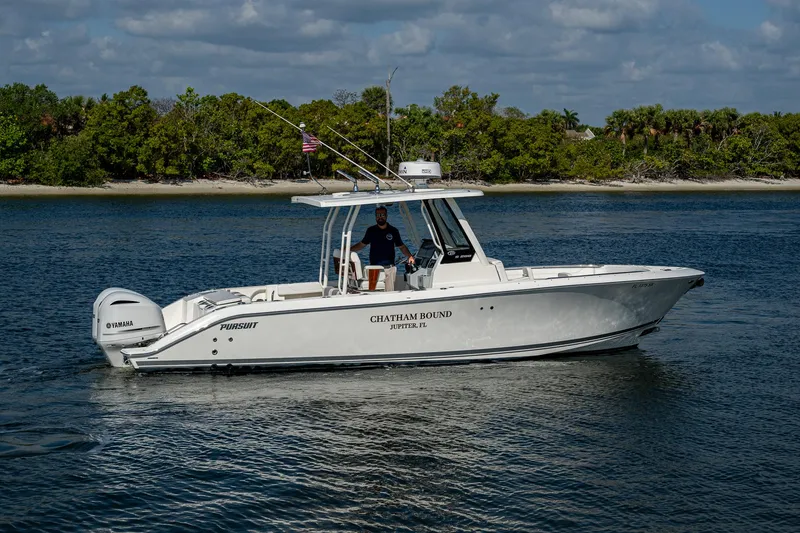 Slide: The Image of 2021 Pursuit S 288 Sport boat on calm water near a forested shoreline. - 18