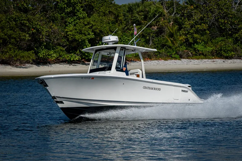 Slide: The Image of 2021 Pursuit S 288 Sport boat cruising on water near a lush shoreline. - 5