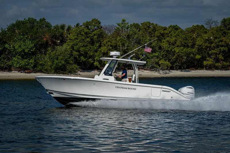Slide: The Image of 2021 Pursuit S 288 Sport boat cruising on water near a forested shoreline. - 7