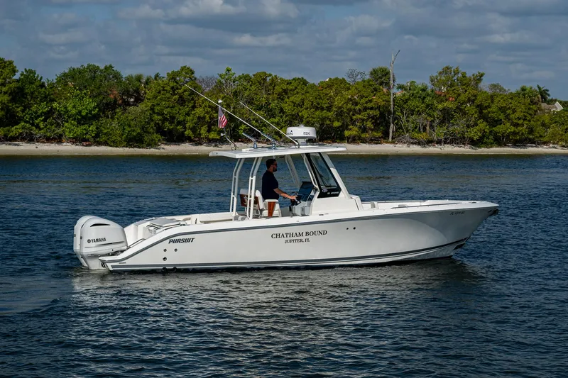 Slide: The Image of 2021 Pursuit S 288 Sport boat cruising on calm water near a forested shoreline. - 8