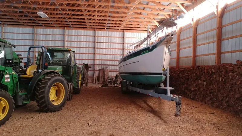 Slide: The Image of 2005 Hake Seaward 32RK sailboat stored in a barn alongside a green tractor. - 4