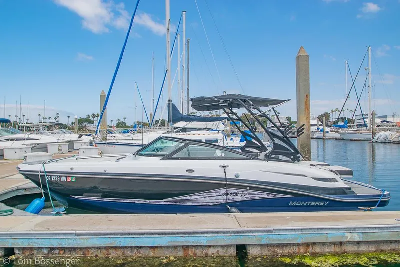 The Image of 2018 Monterey MX6 Surf Edition boat docked at marina, clear sky, sailboats in background. - 1