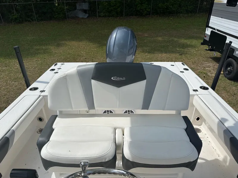 Slide: The Image of 2023 Robalo 226 Cayman boat interior with cushioned seating and motor, parked on grass. - 15