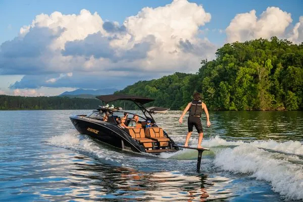Slide: The Image of 2025 Yamaha Boats 255XD on lake with wakeboarder, surrounded by lush greenery and blue sky. - 6