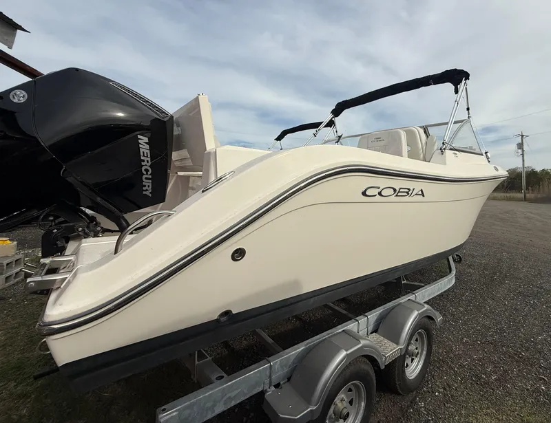 Slide: The Image of 2021 Cobia 220 Dual Console boat on trailer, featuring a Mercury outboard motor. - 2