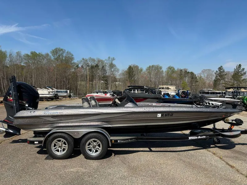 The Image of 2012 Triton 21 HP boat on trailer in outdoor lot, surrounded by trees and other boats. - 1