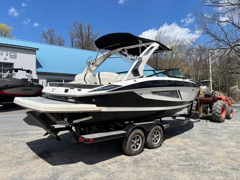 Slide: The Image of 2019 Regal 25 RX Surf boat on trailer, parked outdoors under clear blue sky. - 6