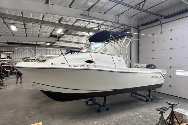 Slide: The Image of 2005 Polar 2300 boat in a garage, white hull, blue canopy, on stands. - 1