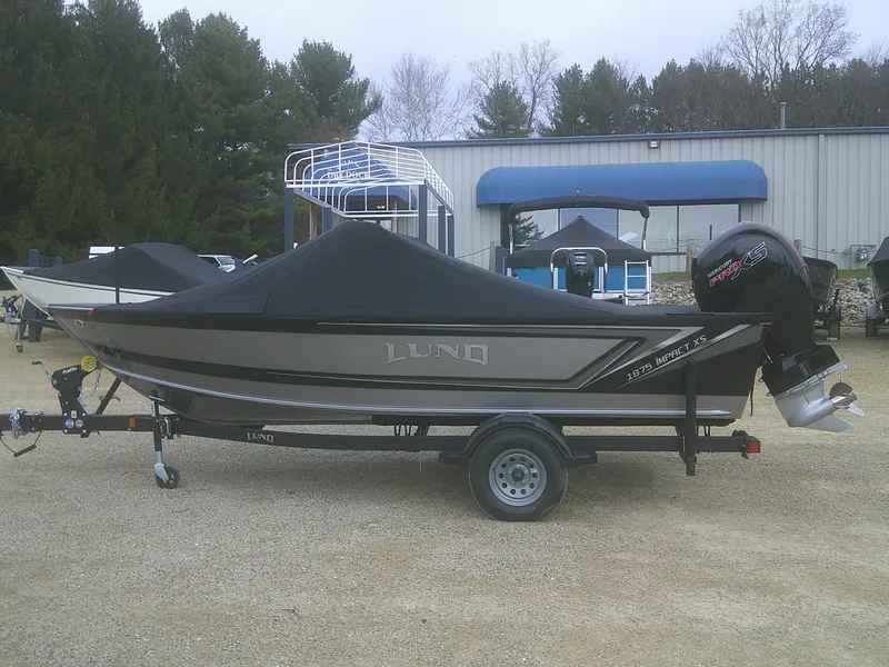 Slide: The Image of 2025 Lund 1875 Impact XS Sport boat on trailer, covered, outdoors. - 26