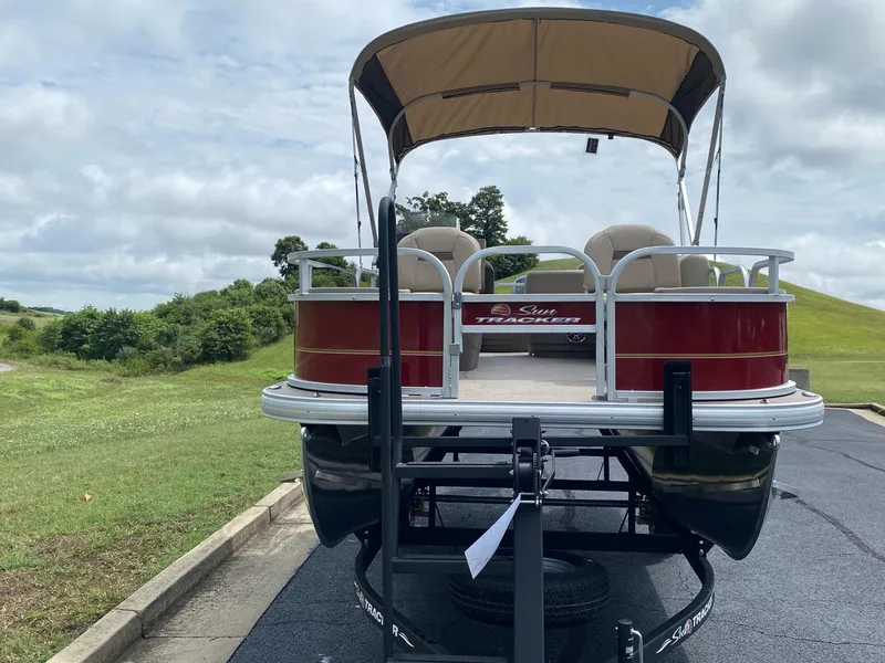 Slide: The Image of 2025 Sun Tracker Bass Buggy 18 DLX pontoon boat on trailer, parked outdoors. - 2