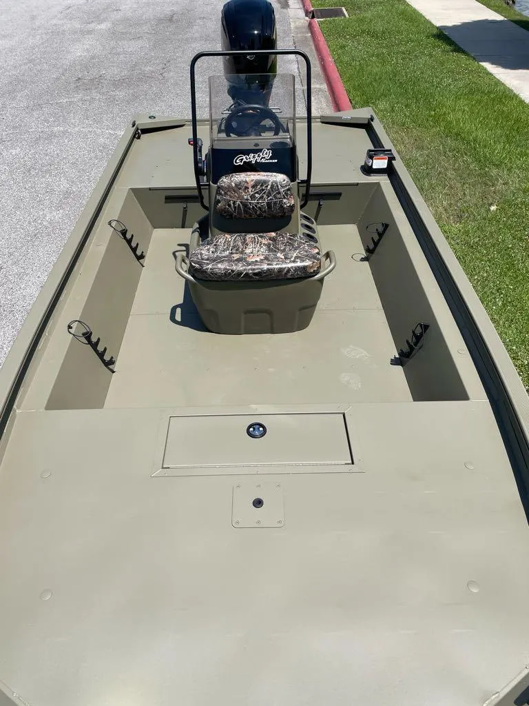 Slide: The Image of 2025 Tracker Grizzly 1860 CC boat with camouflage seating, parked on a street. - 3