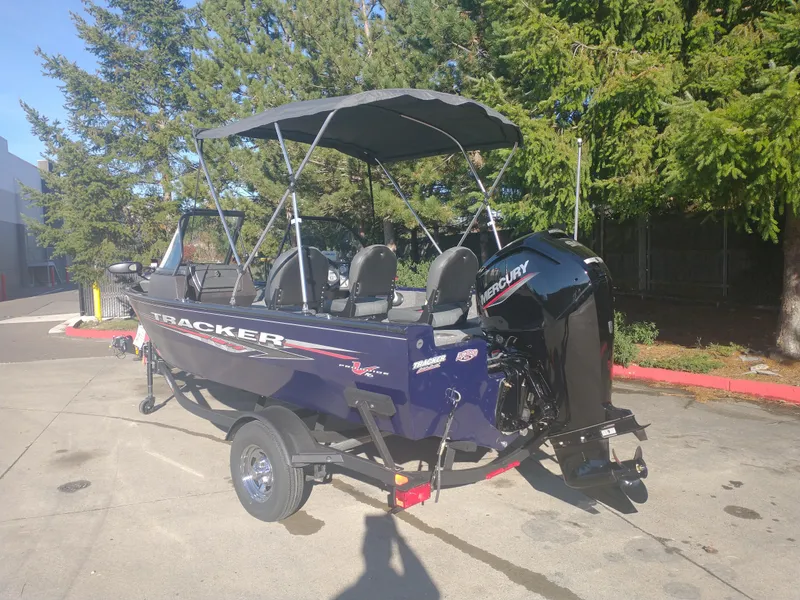 Slide: The Image of 2025 Tracker Pro Guide V-16 WT boat with canopy, parked outdoors. - 2