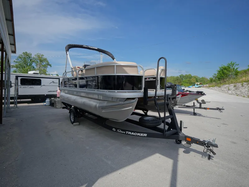 Slide: The Image of 2025 Sun Tracker Party Barge 16 DLX pontoon boat on trailer, parked outdoors. - 13