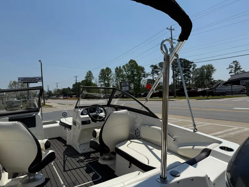 Slide: The Image of 2020 Stingray 191 DC boat interior with seating and steering, parked near a road. - 33