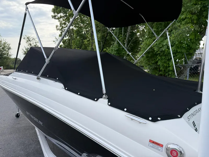 Slide: The Image of 2020 Stingray 191 DC boat with black cover and canopy, parked outdoors. - 40