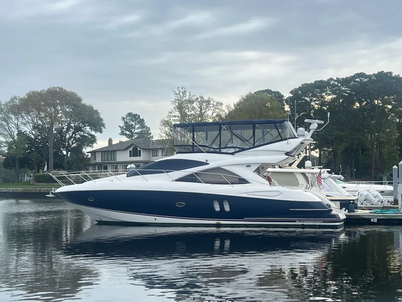 Slide: The Image of 2008 Sunseeker Manhattan 50 yacht docked on calm water, surrounded by trees and houses. - 0