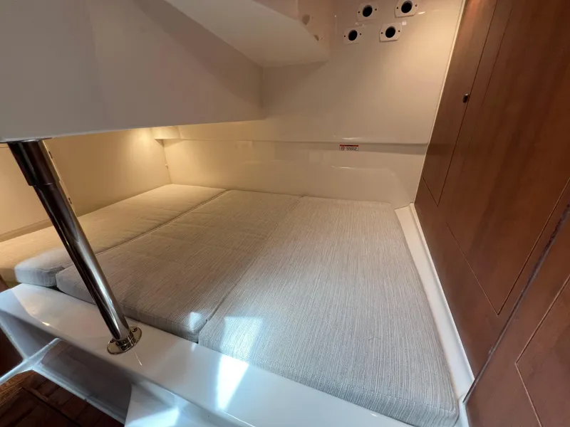 Slide: The Image of 2025 Pursuit OS 325 Offshore cabin interior with cushioned bed and wooden cabinetry. - 25