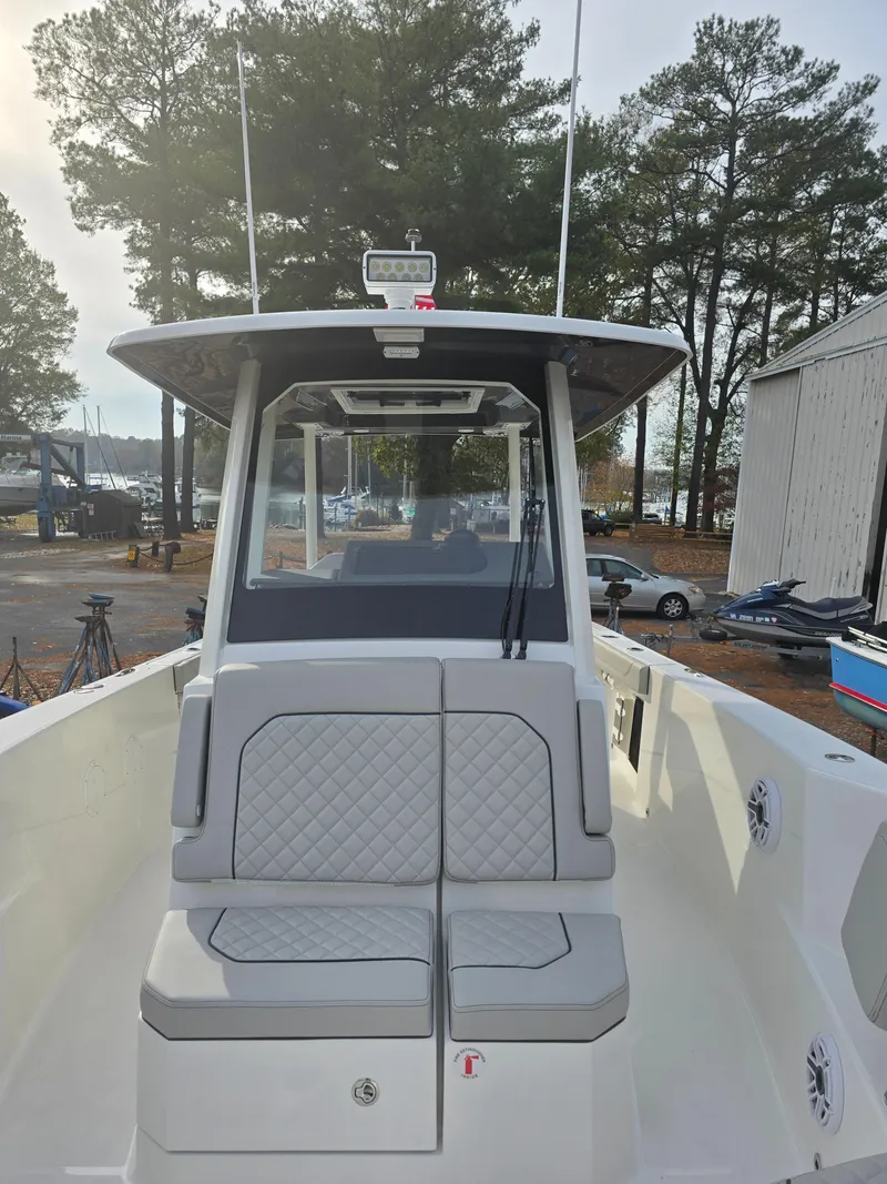 Slide: The Image of 2025 Pursuit S 288 boat with cushioned seating, docked near trees and a marina. - 14
