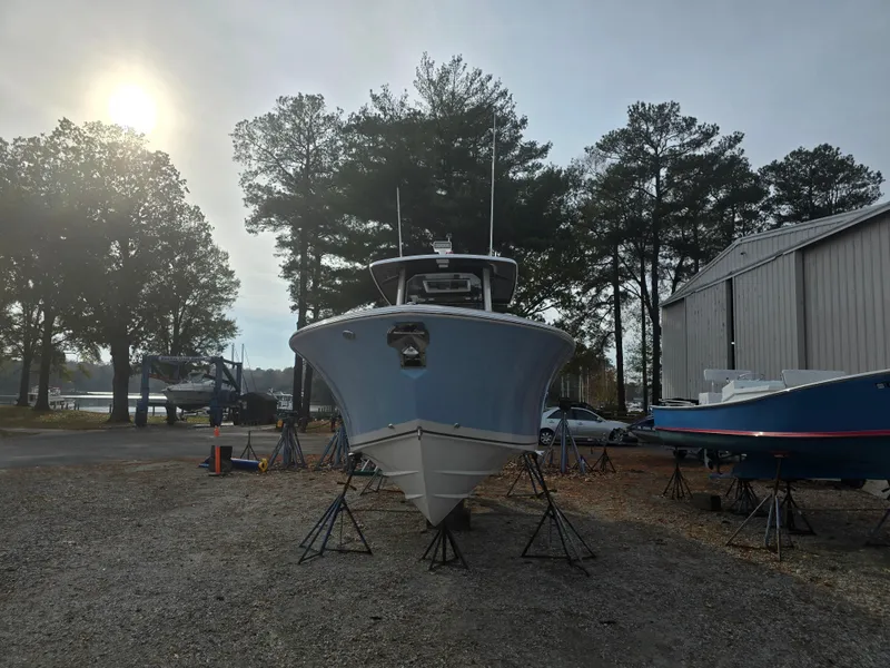 Slide: The Image of 2025 Pursuit S 288 boat on stands, outdoor storage, trees and building in background. - 8