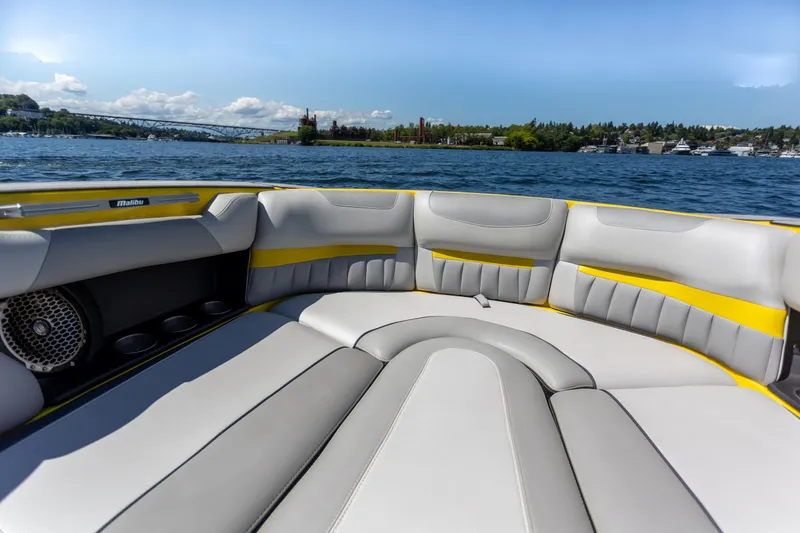 Slide: The Image of 2016 Malibu 24.5 MKZ boat interior with gray and yellow seating on a sunny lake. - 20