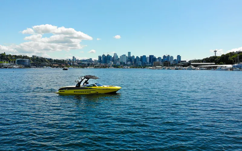 Slide: The Image of Yellow 2016 Malibu 24.5 MKZ boat on water with city skyline in background. - 38
