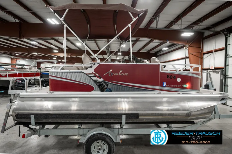 Slide: The Image of 2019 Avalon Eagle pontoon boat in showroom, featuring red and silver design, on trailer. - 7