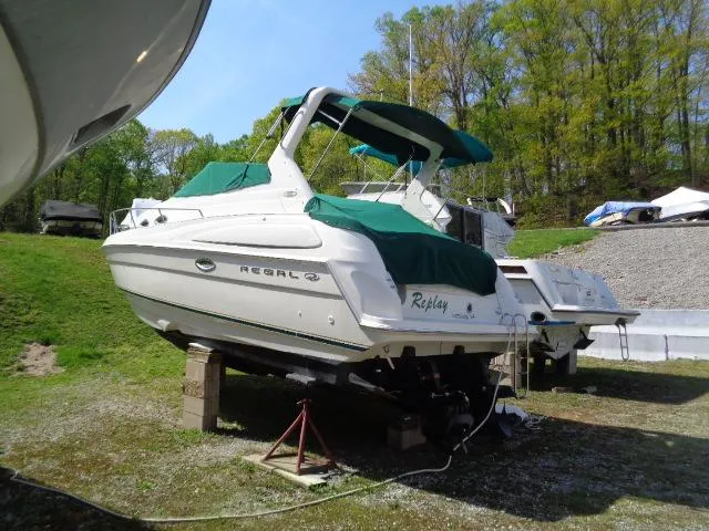 Slide: The Image of 2001 Regal Commodore 2760 boat on dry dock with green canopy, surrounded by trees. - 2