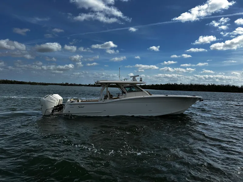 Slide: The Image of 2025 Scout 400 LXF boat cruising on a sunny day with scattered clouds. - 2