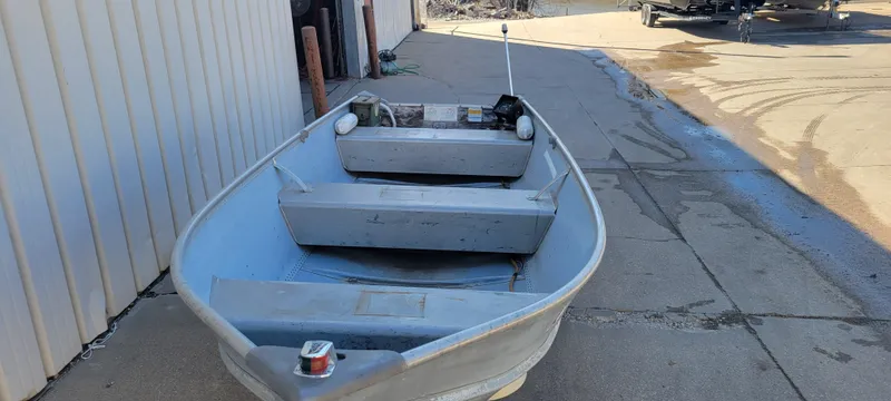 Slide: The Image of 1988 Lowe 14' V boat on concrete near building, showing interior seating and equipment. - 2