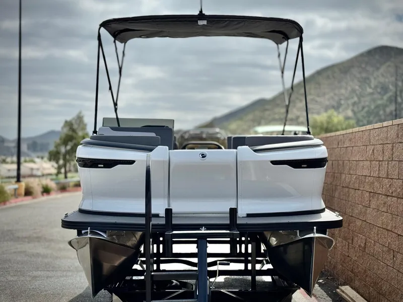 Slide: The Image of 2025 Manitou Cruise 20 Bench Twin Tube pontoon boat, rear view, with scenic mountain backdrop. - 2