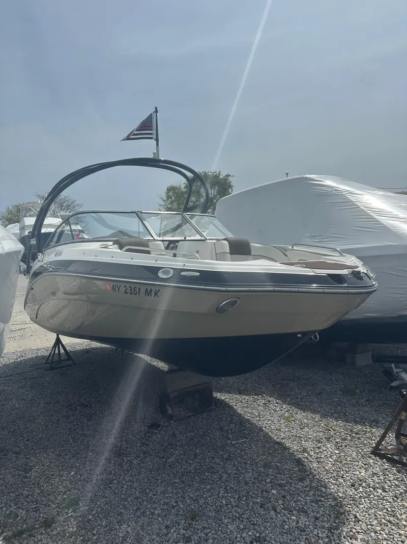 Slide: The Image of 2013 Yamaha Boats 242 Limited S on display, parked on gravel, with a flag above. - 0