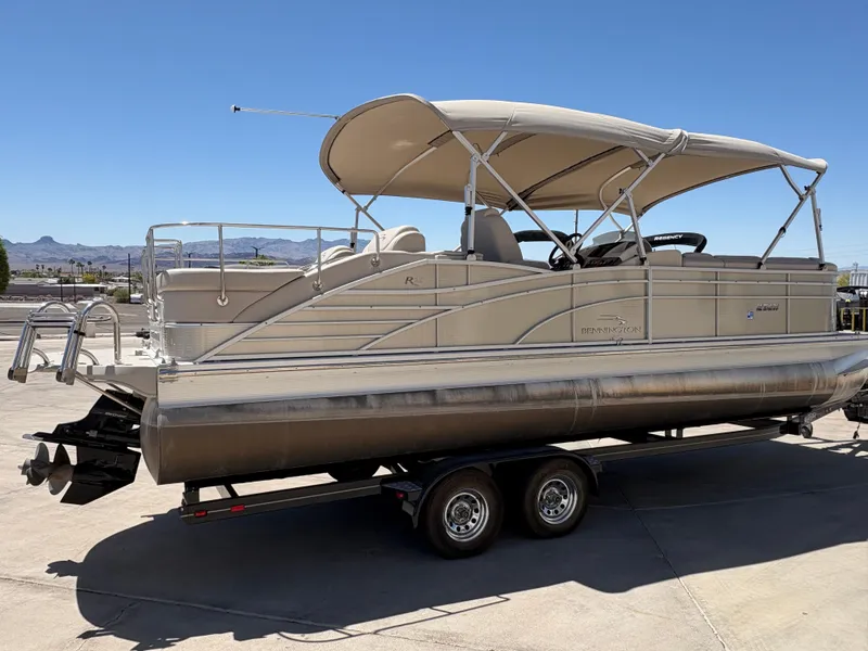 Slide: The Image of 2013 Bennington 2575 RCW IO pontoon boat on trailer, beige canopy, sunny day. - 2