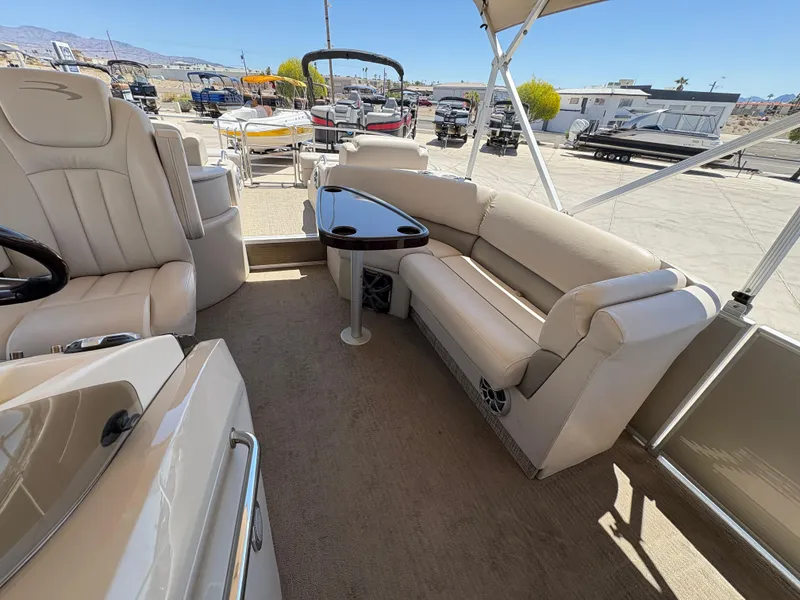 Slide: The Image of 2013 Bennington 2575 RCW IO boat interior with beige seating and table, parked outdoors. - 6