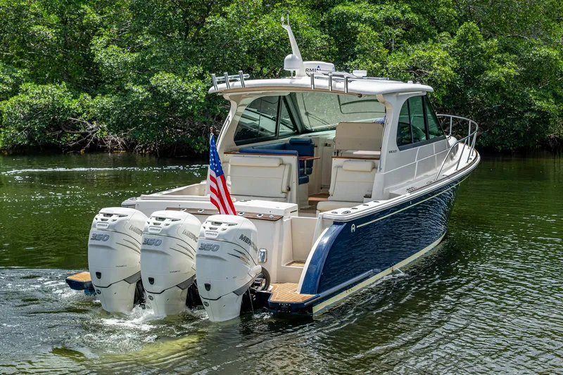 Slide: The Image of 2021 Hinckley Sport Boat 40 X with triple outboard engines on a serene waterway. - 3