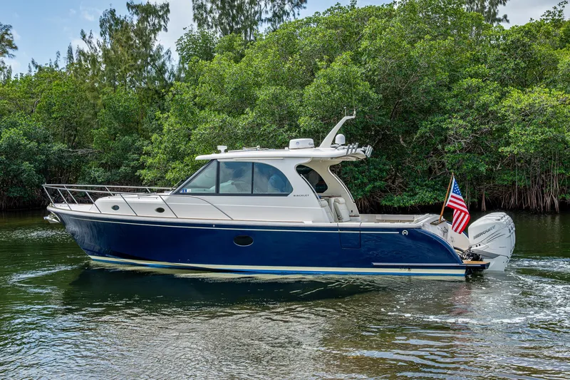 Slide: The Image of 2021 Hinckley Sport Boat 40 X cruising on a serene waterway, surrounded by lush greenery. - 33