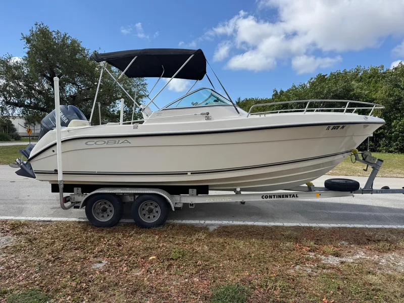 Slide: The Image of 2011 Cobia 215 Dual Console boat on trailer, parked outdoors under a blue sky. - 6