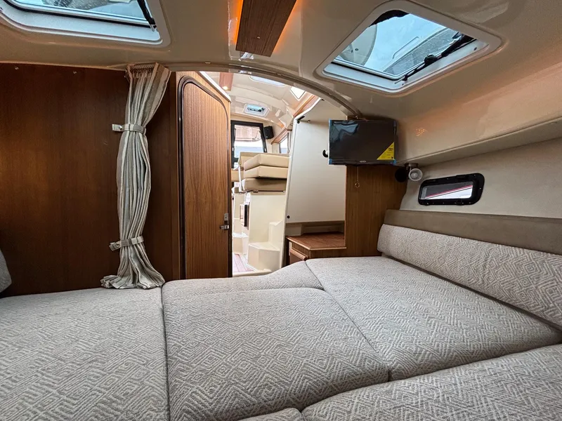 Slide: The Image of 2025 Ranger Tugs R-25 interior cabin with cozy bed, wood accents, and natural light. - 12