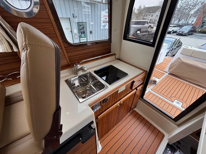 Slide: The Image of 2025 Ranger Tugs R-25 interior with compact kitchen, featuring sink and stove, wood finish. - 9