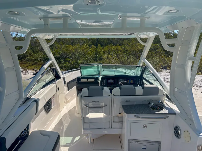 Slide: The Image of 2024 Chaparral 280 OSX boat interior with seating and helm, surrounded by lush greenery. - 11