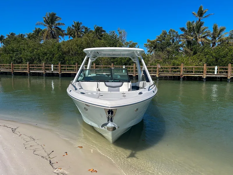 Slide: The Image of 2024 Chaparral 280 OSX boat docked on a sandy shore, surrounded by lush greenery. - 3