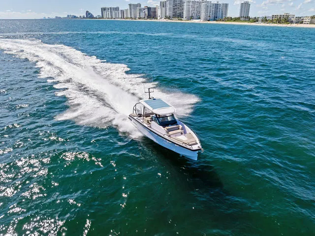 Slide: The Image of 2026 Axopar 29 Sun-Top boat cruising on a scenic blue lake with shoreline houses. - 28