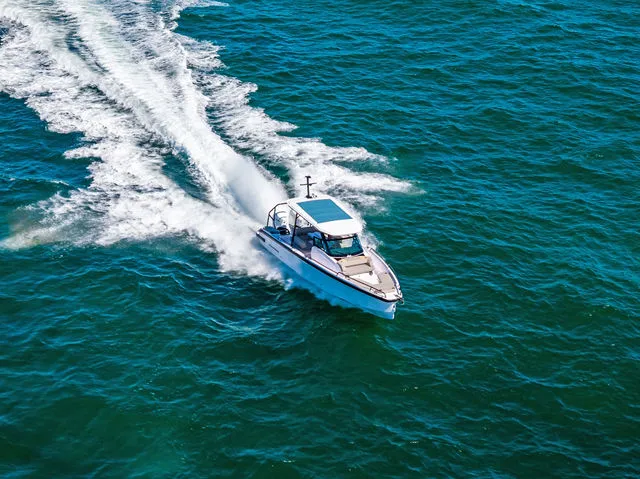 Slide: The Image of 2026 Axopar 29 Sun-Top boat cruising near a wooded shoreline. - 30