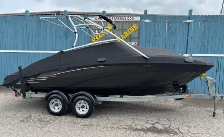 Slide: The Image of 2012 Yamaha AR210 boat on trailer, covered, parked by blue fence. - 39