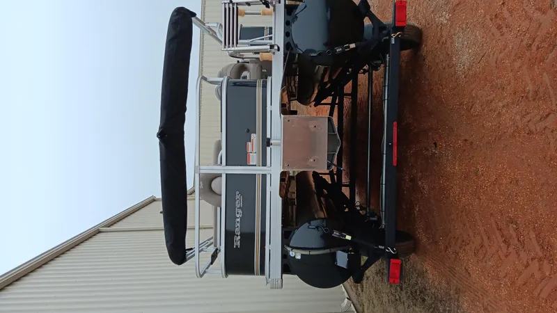 Slide: The Image of 2022 Ranger 200F boat on trailer, parked on red dirt near a building. - 13