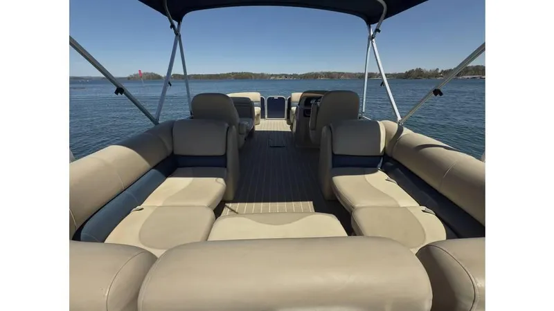 Slide: The Image of 2019 Manitou 23 Aurora LE Bar pontoon boat interior with beige seating on a lake. - 7