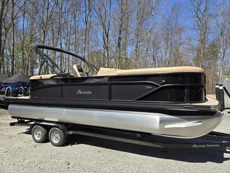 Slide: The Image of 2025 Barletta C22QC pontoon boat on trailer, parked outdoors, surrounded by trees. - 4