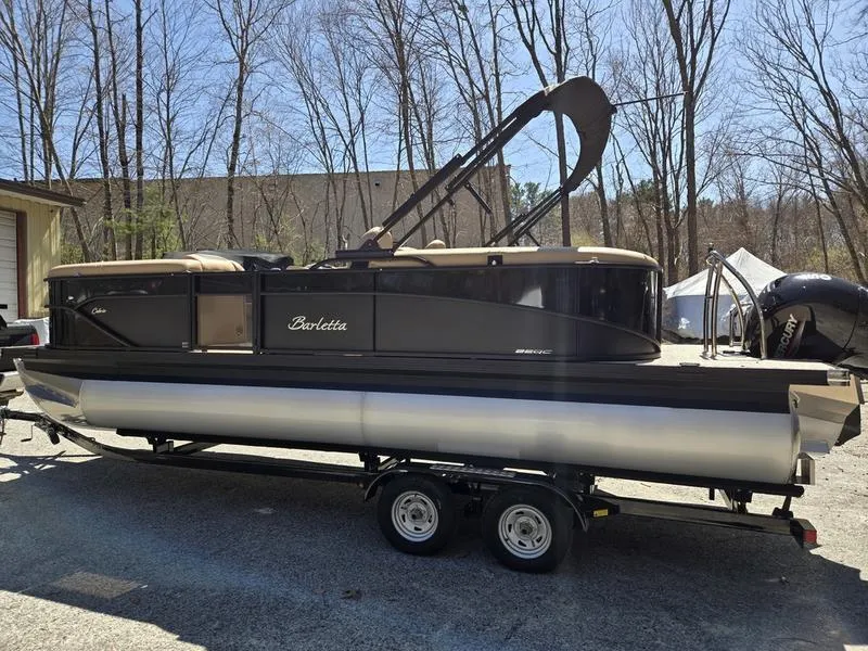 Slide: The Image of 2025 Barletta C22QC pontoon boat on trailer, parked outdoors, surrounded by trees. - 5