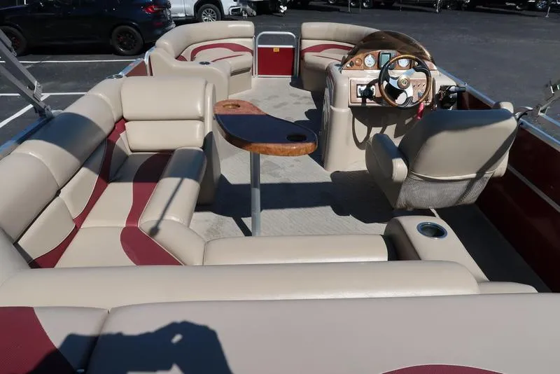 Slide: The Image of 2012 Berkshire G210CL pontoon boat interior with beige and red seating, wooden table, and steering console. - 16