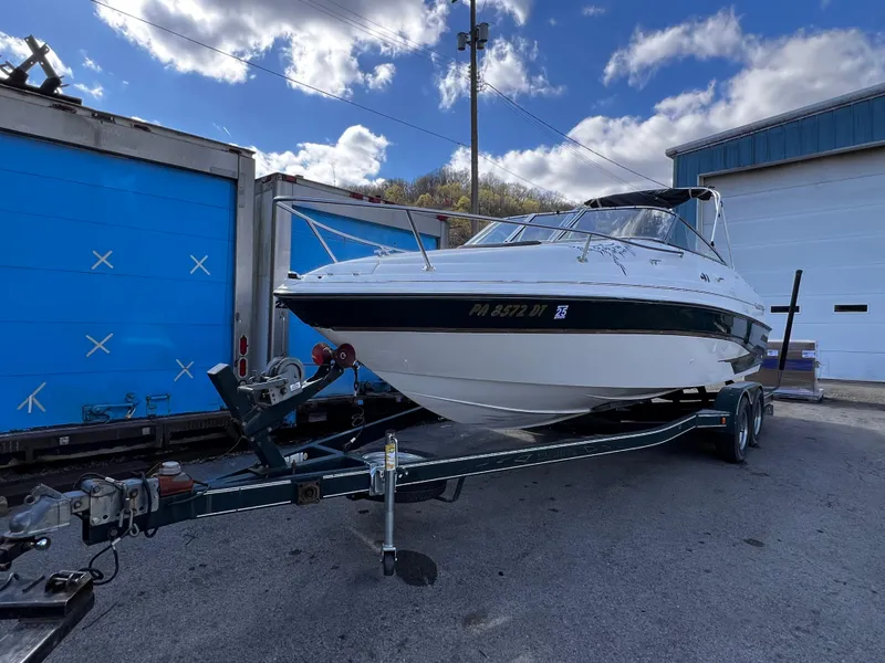 Slide: The Image of 2001 Glastron GS 229 boat on trailer, parked outdoors near blue garage doors. - 2